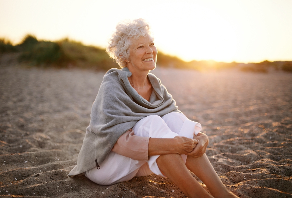 Happy,Retired,Woman,Wearing,Shawl,Sitting,Relaxed,On,Sand,At