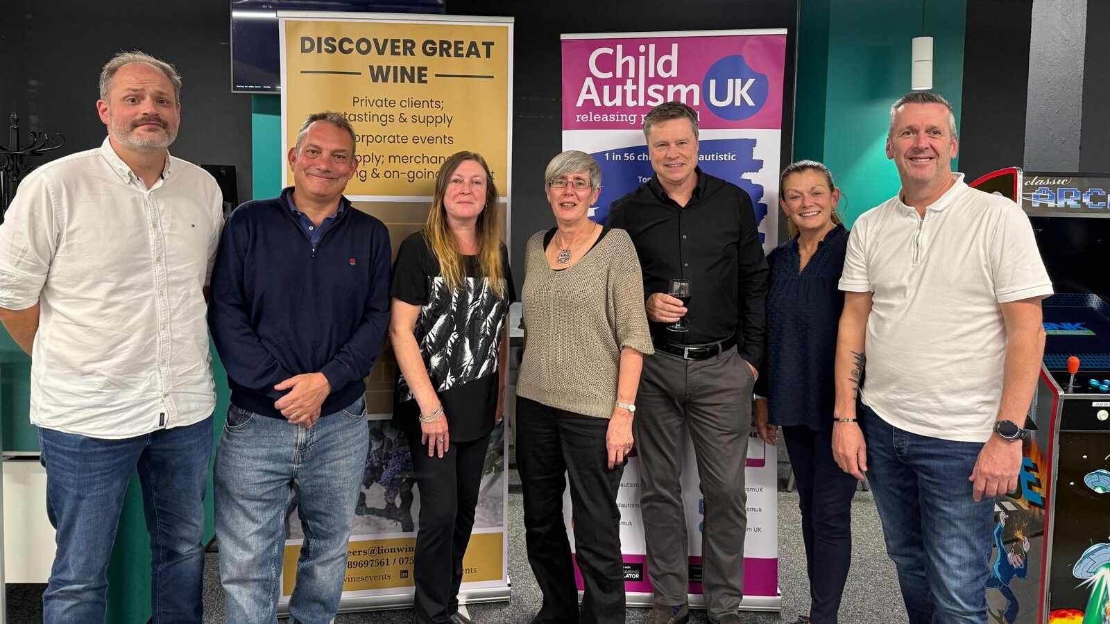 Six people stand in front of banners for Child Autism UK and LION wines
